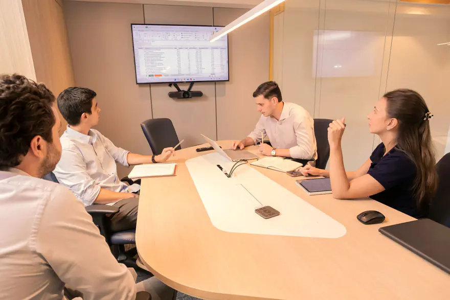 Equipe em reunião ao redor de uma mesa com uma tela ligada na parede