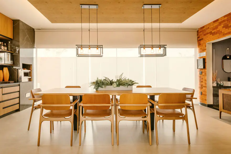 Sala de jantar clara com persianas fechadas e dois pendentes acesos sobre a mesa de madeira