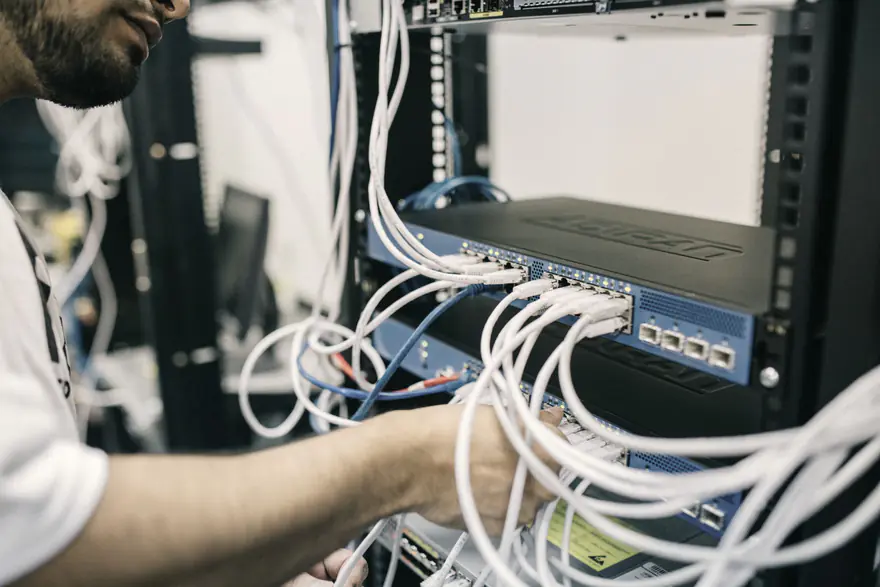 Mãos de um técnico organizando cabos de rede brancos ligados a um switch dentro de um rack