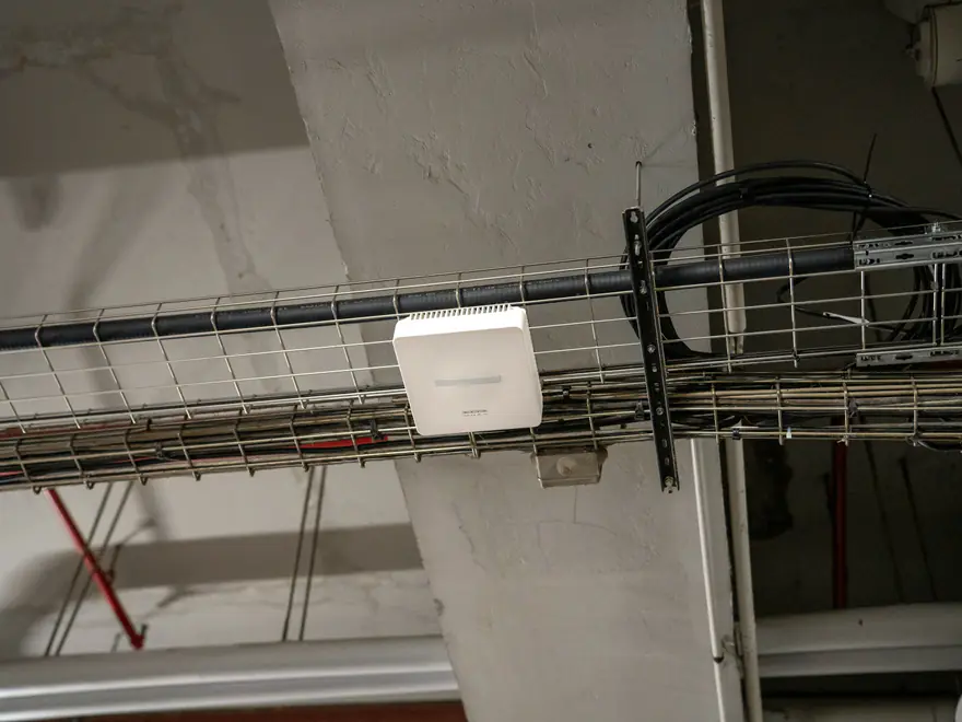 Ponto de acesso Wi-Fi branco preso a uma calha de cabos no teto